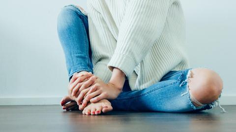 Eine Frau sitzt auf dem Boden und umfasst ihre nackten Füße.