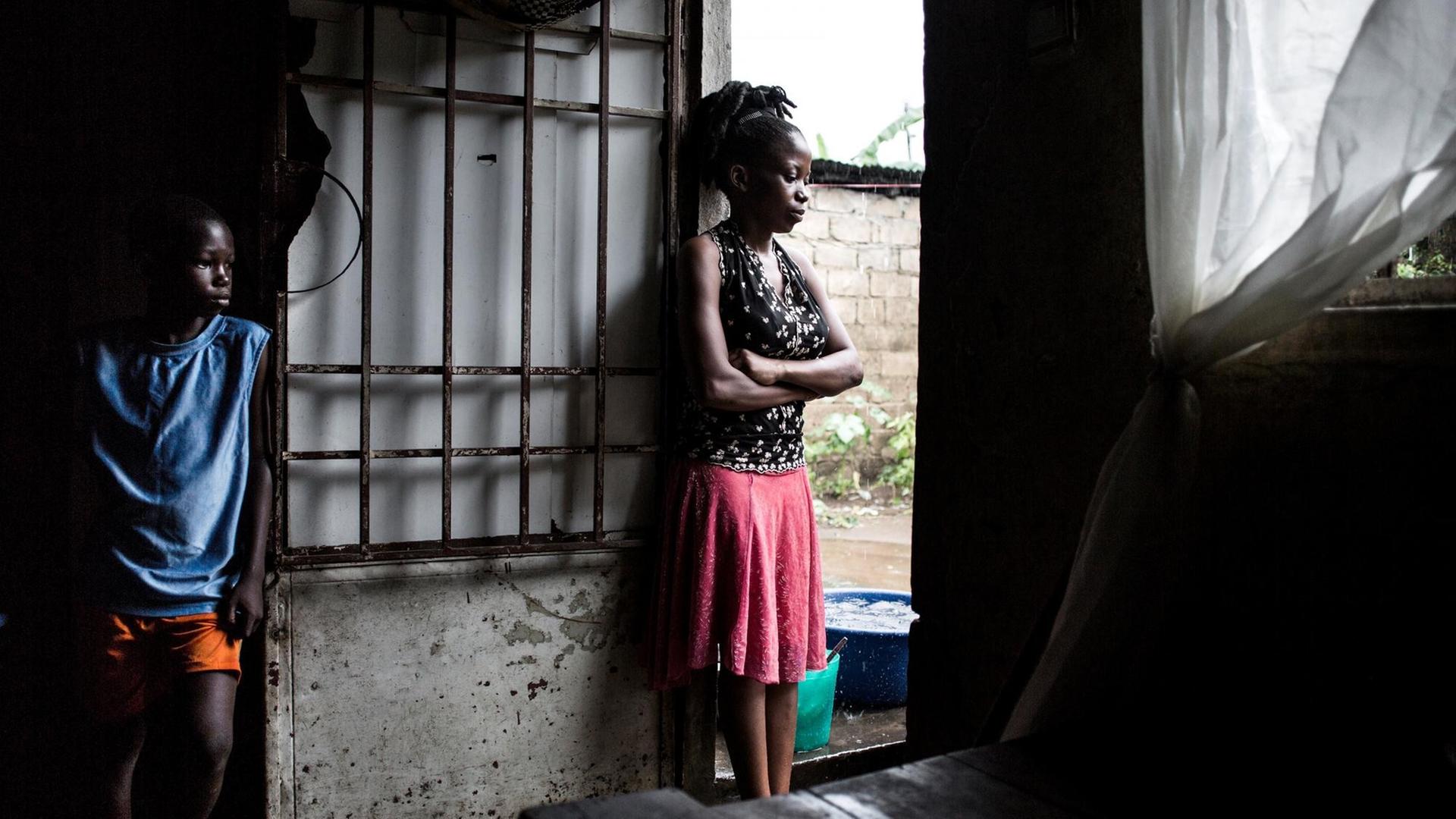 Im Kongo breitet sich die Cholera aus. Zwei junge Menschen stehen in einer Hütte in einem Slum und blicken durch die offene Tür nach draußen. Im Kongo breitet sich die Cholera aus. Zwei junge Menschen stehen in einer Hütte in einem Slum und blicken durch die offene Tür nach draußen.