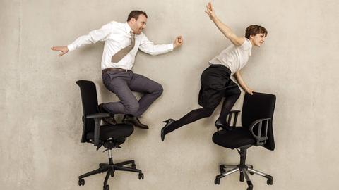 Zwei gehetzte Büroarbeiter balancieren auf Bürostühlen