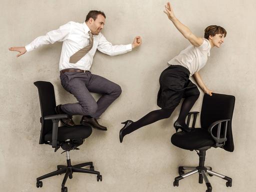 Zwei gehetzte Büroarbeiter balancieren auf Bürostühlen