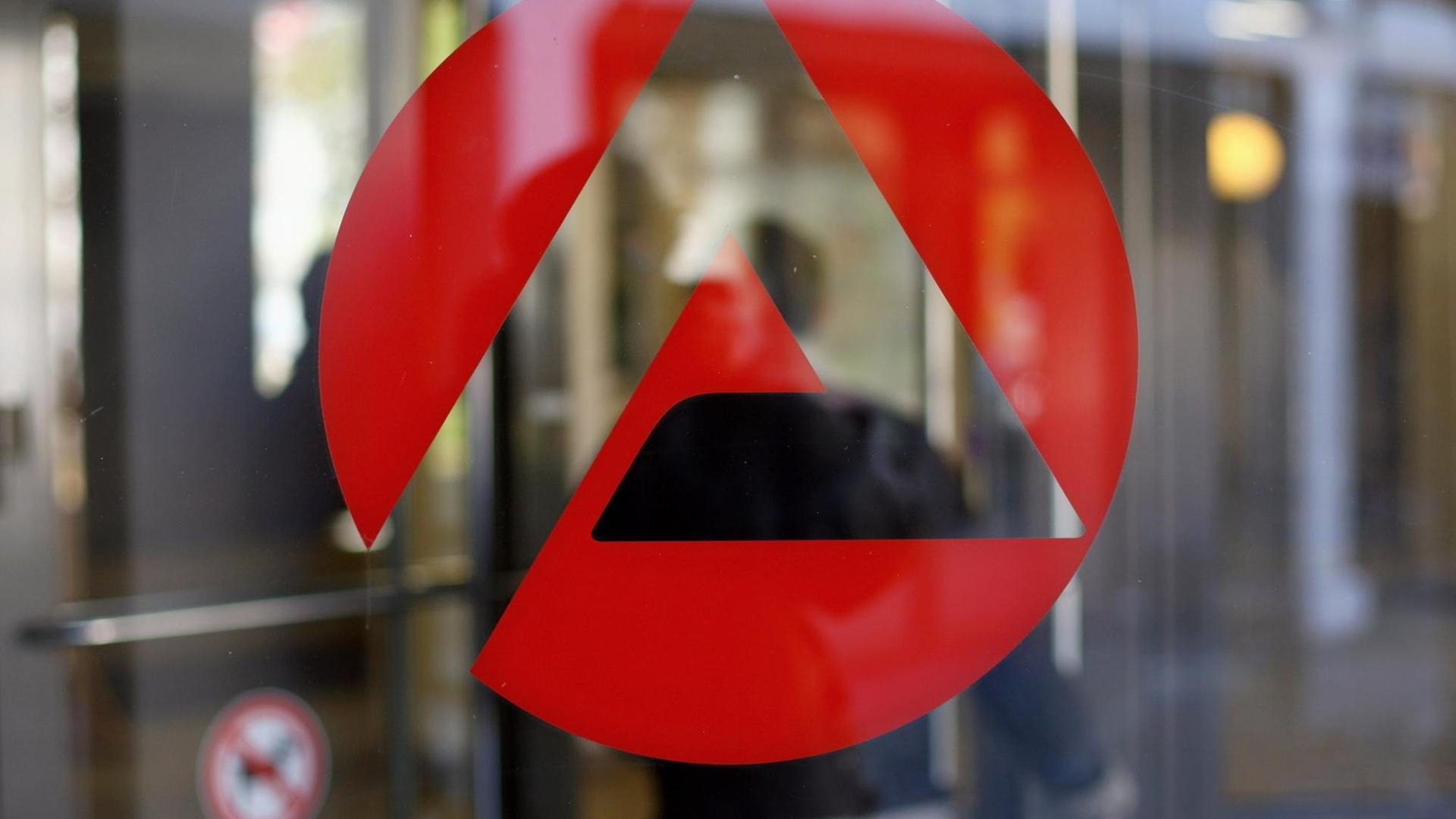 Auf einer Scheibe klebt das rote Logo des Jobcenter, im Hintergrund in der Unschärfe betritt ein Mann das Gebäude. Auf einer Scheibe klebt das rote Logo des Jobcenter, im Hintergrund in der Unschärfe betritt ein Mann das Gebäude.