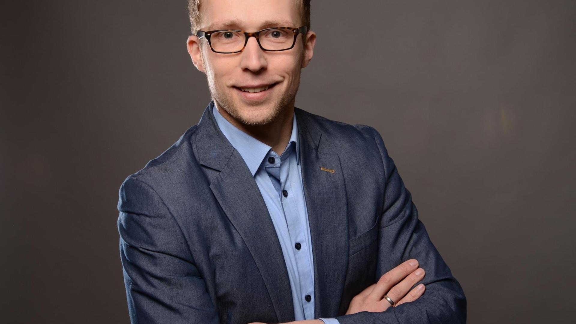 Dr. Matthias Braun steht vor grauem Hintergrund im Studio. Er trägt ein Jeanssakko und hat die Arme verschränkt. Dr. Matthias Braun steht vor grauem Hintergrund im Studio. Er trägt ein Jeanssakko und hat die Arme verschränkt.