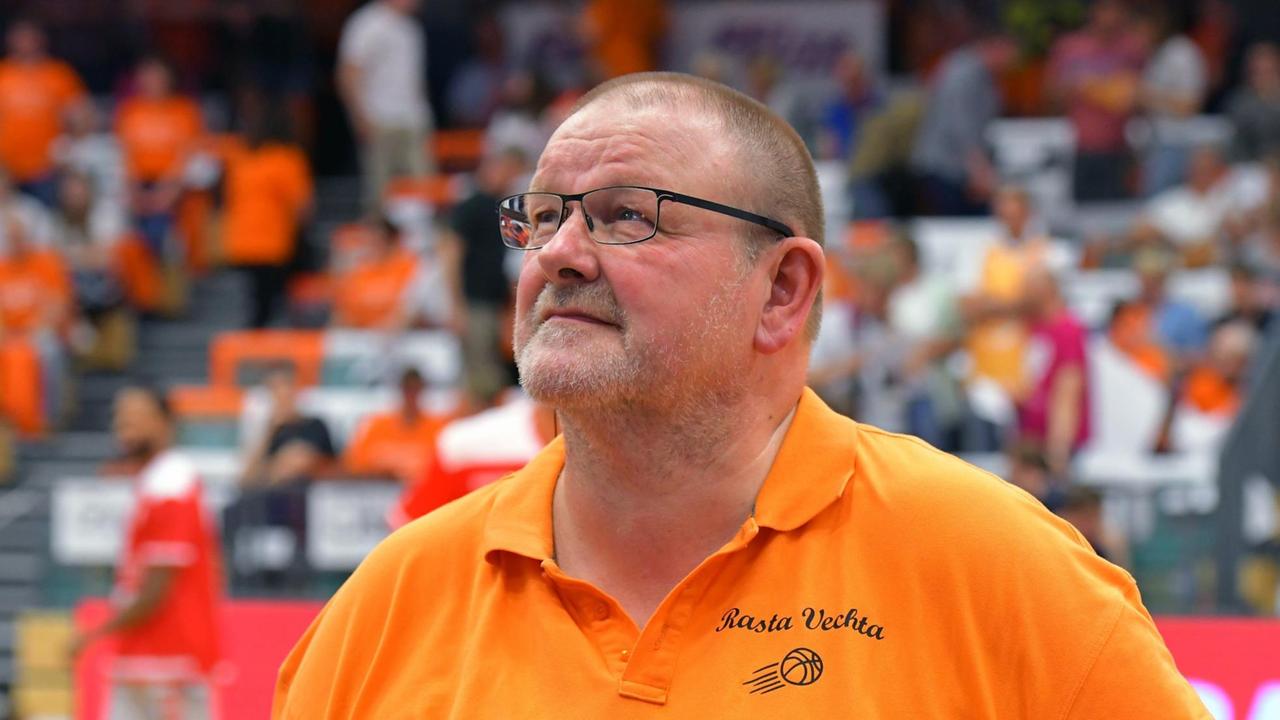Geschäftsführer Stefan Niemeyer vom SC Rasta Vechta in einem orangefarbenen Polohemd. Im Hintergrund sind Zuschauerränge mit Menschen zu sehen. Geschäftsführer Stefan Niemeyer vom SC Rasta Vechta in einem orangefarbenen Polohemd. Im Hintergrund sind Zuschauerränge mit Menschen zu sehen.