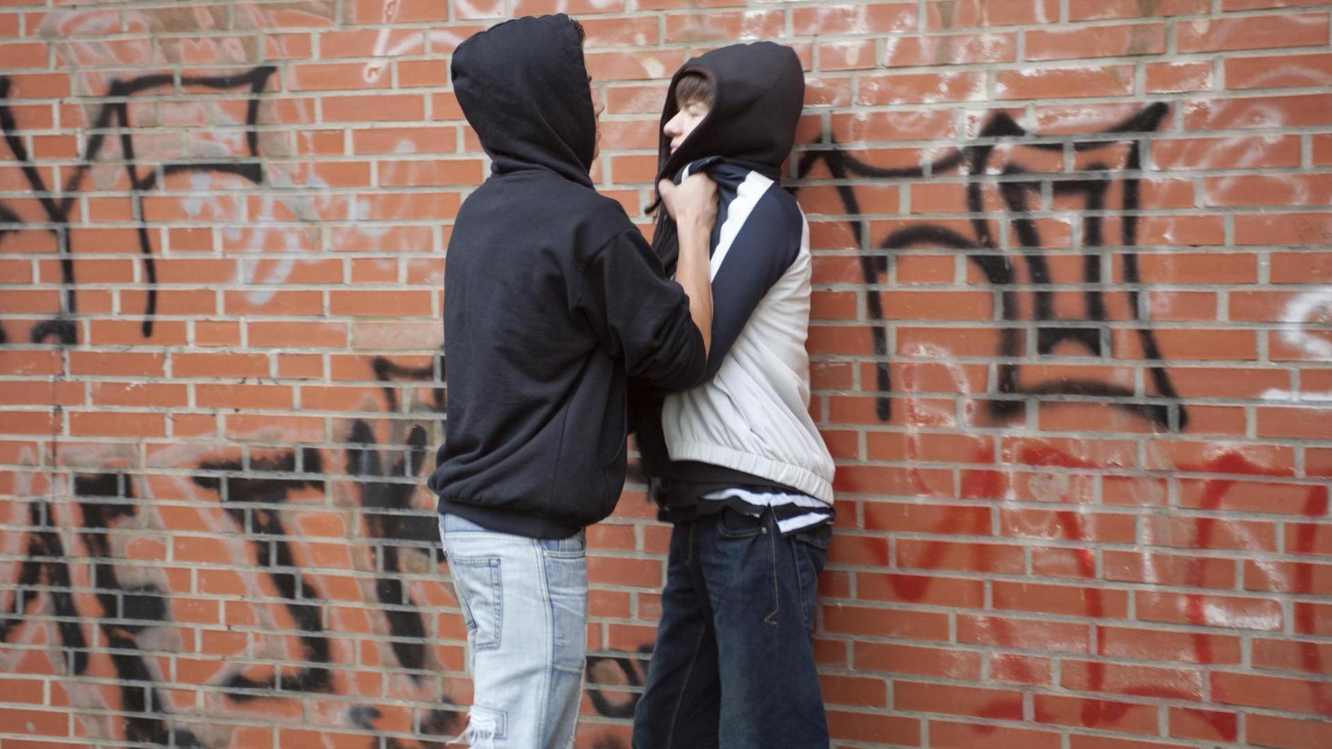 Ein Teenager drückt einen kleineren gewaltsam gegen eine Wand, gestellte Szene Ein Teenager drückt einen kleineren gewaltsam gegen eine Wand, gestellte Szene