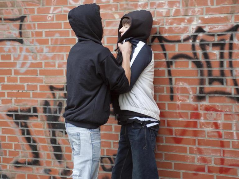 Ein Teenager drückt einen kleineren gewaltsam gegen eine Wand, gestellte Szene
