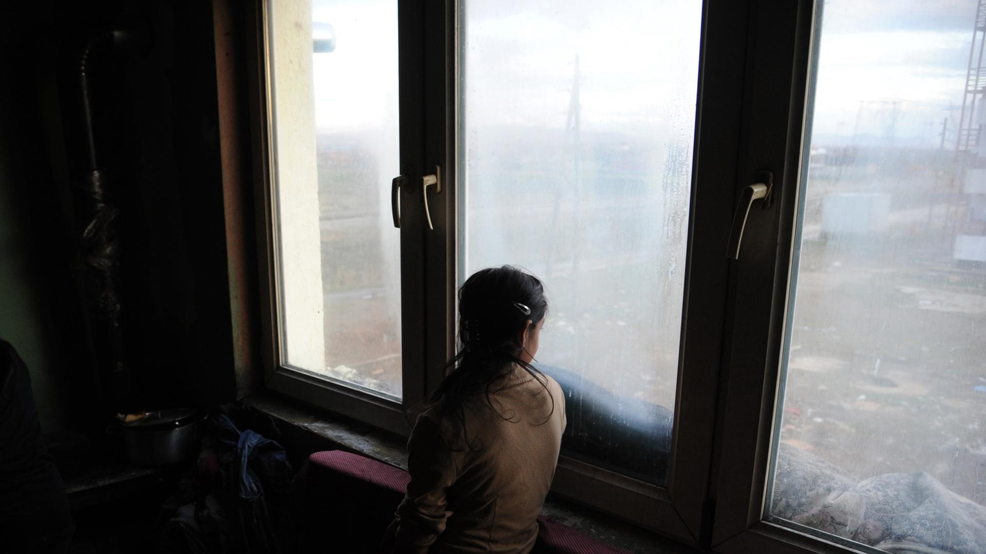 Eine Mädchen schaut Plementina bei Pristina im Kosovo aus dem Fenster einer Wohnung Eine Mädchen schaut Plementina bei Pristina im Kosovo aus dem Fenster einer Wohnung