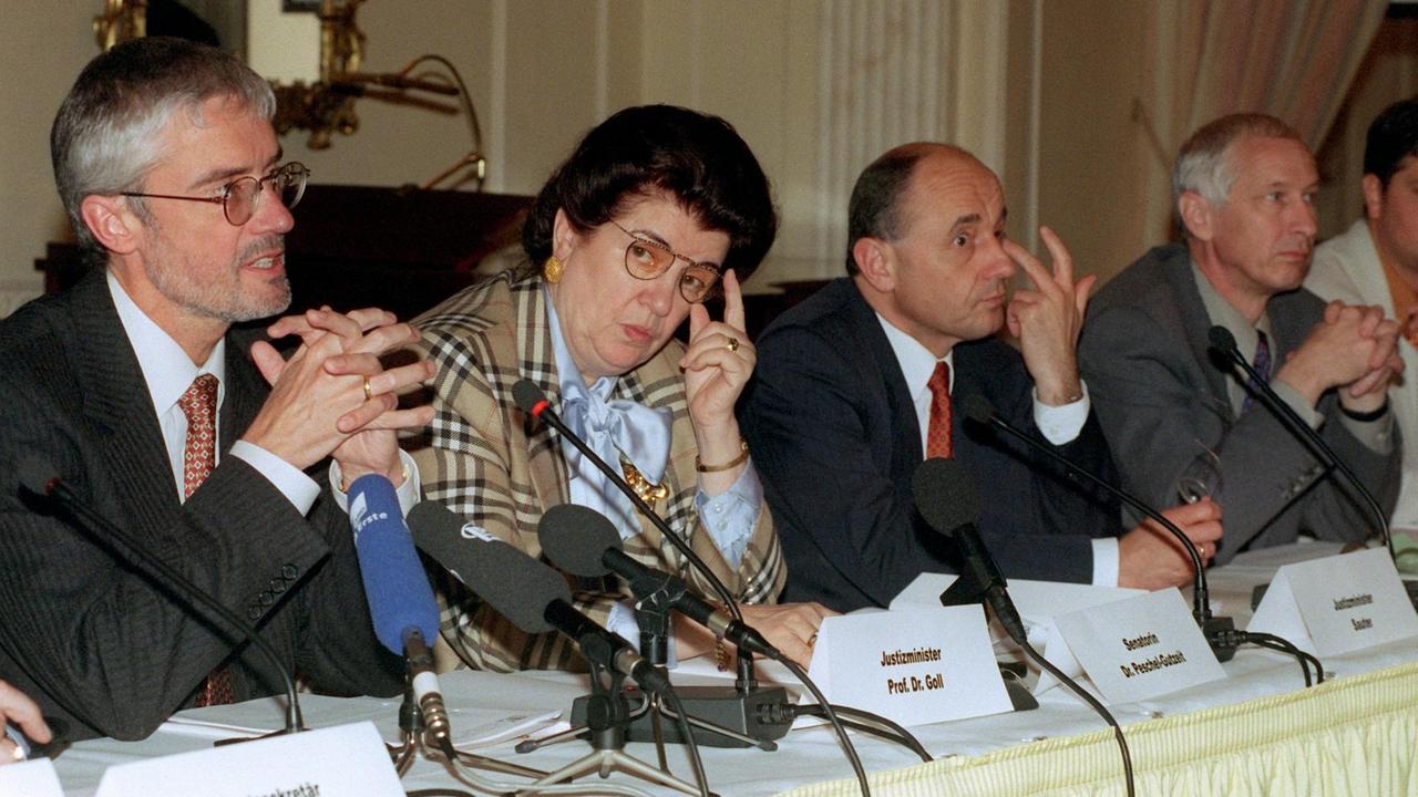 Vier Menschen sitzen bei einer Pressekonferenz vor Mikrofonen. In der Mitte sitzt Lore Peschel-Gutzeit.