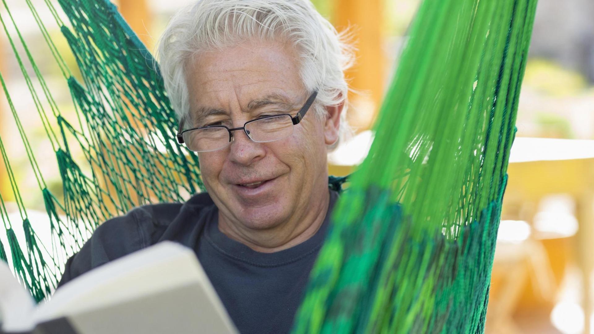 Ein älterer Mann liest in der Hängematte ein Buch Ein älterer Mann liest in der Hängematte ein Buch