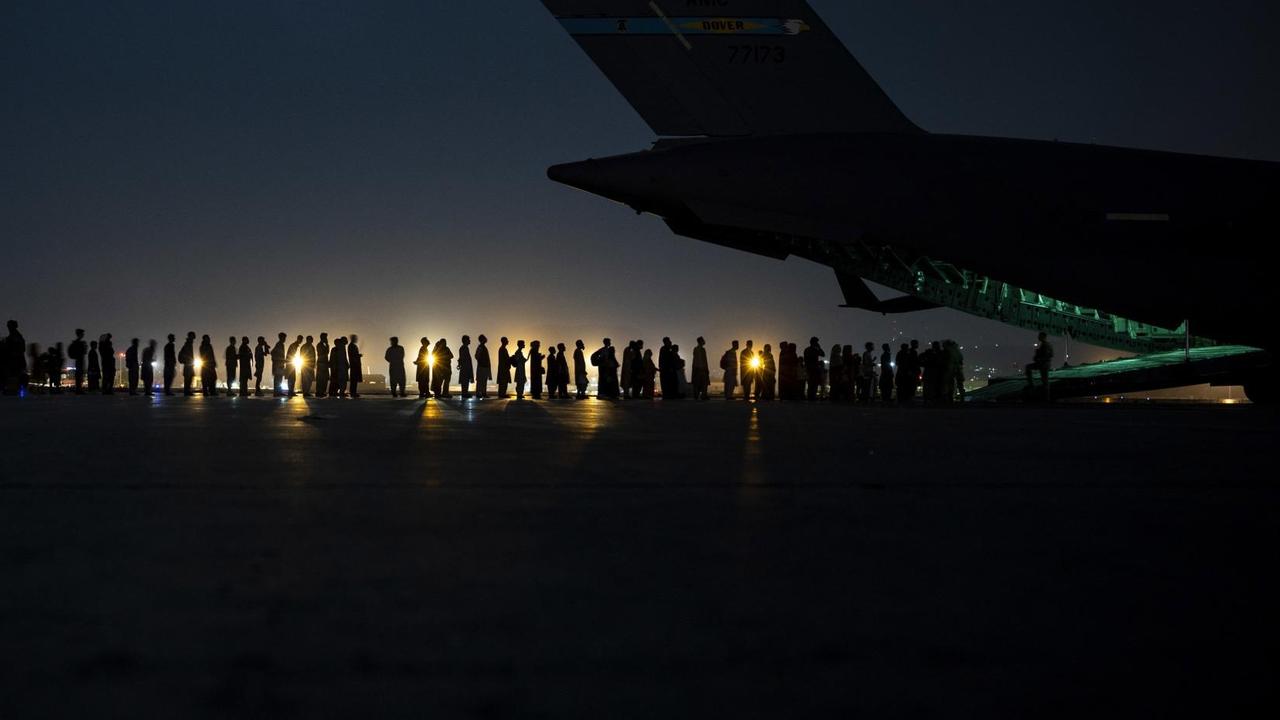 Eine Menschenschlange, die in das geöffnete Heck eines Flugzeugs führt, bei Nacht. Eine Menschenschlange, die in das geöffnete Heck eines Flugzeugs führt, bei Nacht.