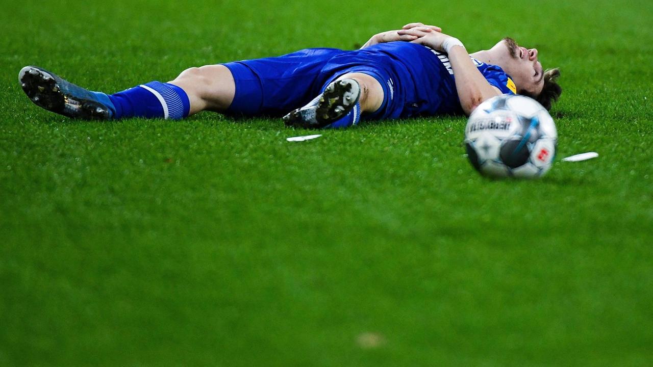Ein Spieler im blauen Trikot liegt auf dem Rasen, neben ihm ein Fußball. Ein Spieler im blauen Trikot liegt auf dem Rasen, neben ihm ein Fußball.