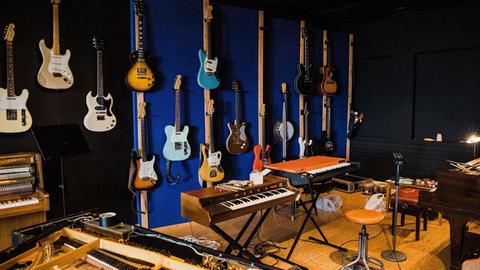 In einem Tonstudio in Reykjavík hängen Gitarren an der Wand, ein offener Flügel steht im Vordergrund, mehrere weitere Tasteninstrumente sind zu sehen, in der Mitte steht ein Hocker.