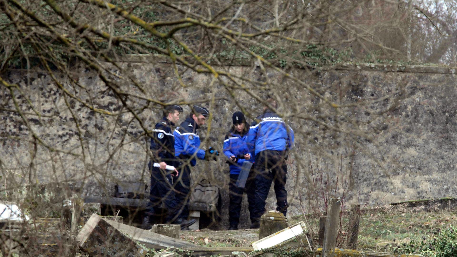 Polizisten stehen vor umgeworfenen Gräbern. Polizisten stehen vor umgeworfenen Gräbern.