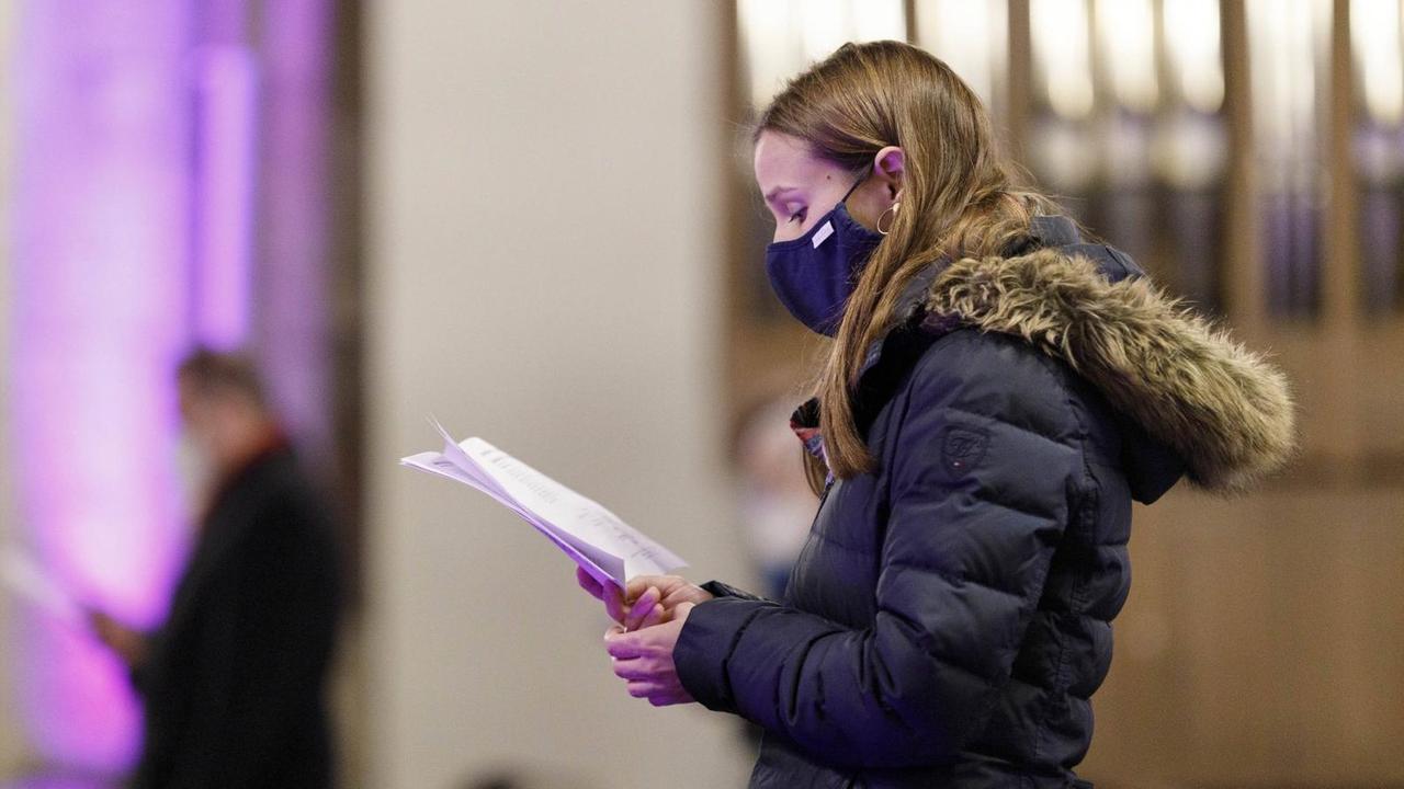 Eine junge Kirchengängerin singt während des Gottesdienstes. Sie trägt einen Mundschutz. Eine junge Kirchengängerin singt während des Gottesdienstes. Sie trägt einen Mundschutz.