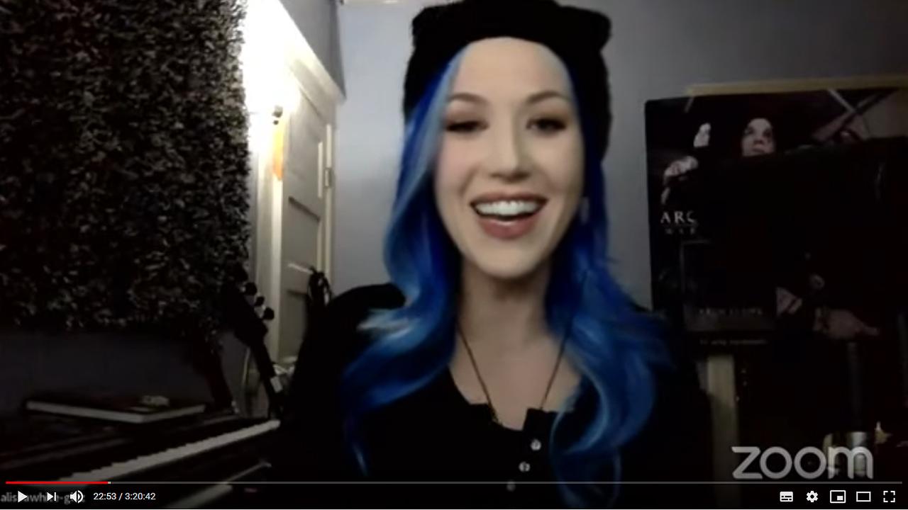 Alissa White-Gluz, Sängerin der Metal-Band Arch Enemy. Eine Frau mit langen blauen Haaren sitzt in einem Zimmer vor einer Kamera.