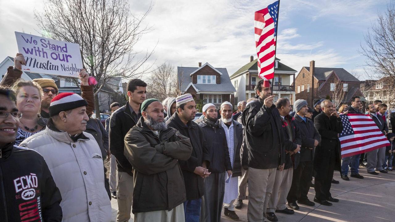 Muslime und Nicht-Muslime stehen mit Schildern und US-Flaggen nebeneinander auf der Straße Muslime und Nicht-Muslime stehen mit Schildern und US-Flaggen nebeneinander auf der Straße