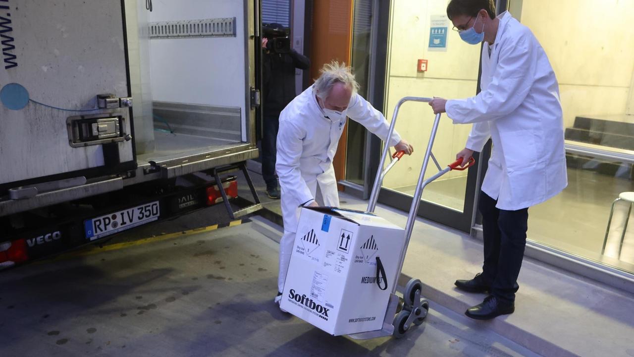 Mitarbeiter transportieren einen Karton mit einigen der ersten knapp 10.000 Dosen Corona-Impfstoff für Thüringen in ein Gebäude. Mitarbeiter transportieren einen Karton mit einigen der ersten knapp 10.000 Dosen Corona-Impfstoff für Thüringen in ein Gebäude.