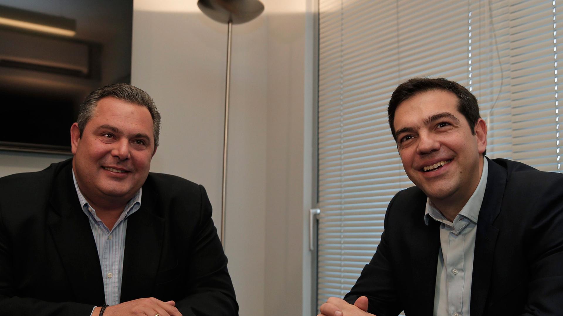 Panos Kammenos und Alexis Tsipras sitzen an einem Tisch und lächeln in die Kameras. Panos Kammenos und Alexis Tsipras sitzen an einem Tisch und lächeln in die Kameras.