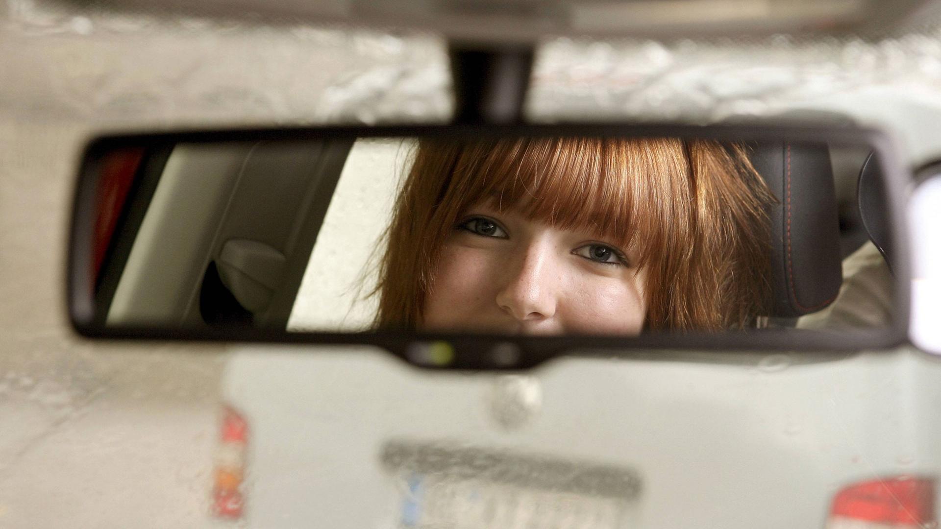 Eine junge Frau schaut in den Rückspiegel.