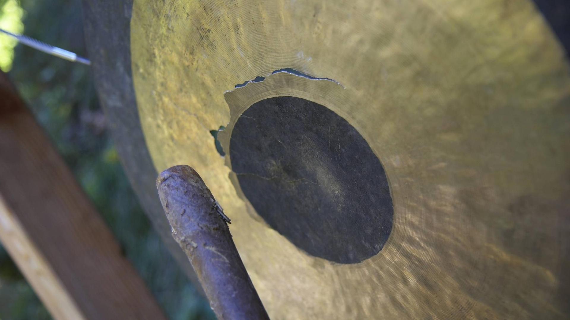 Ein goldfarbener Gong wird mit einem Schlegel aus Holz geschlagen. Ein goldfarbener Gong wird mit einem Schlegel aus Holz geschlagen.