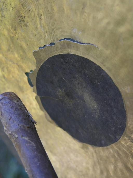 Ein goldfarbener Gong wird mit einem Schlegel aus Holz geschlagen.