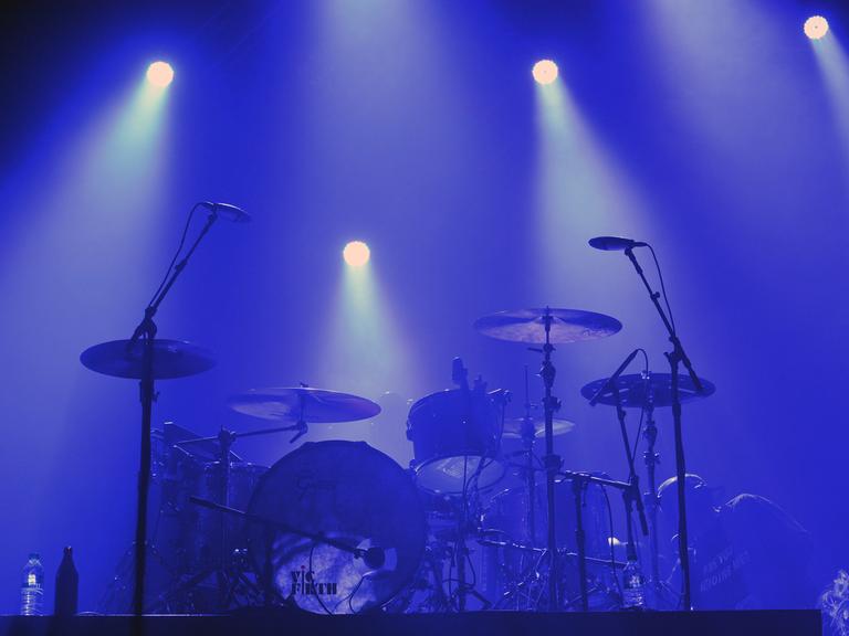 Ein Schlagzeug steht auf einer blau beleuchteten Bühne.  