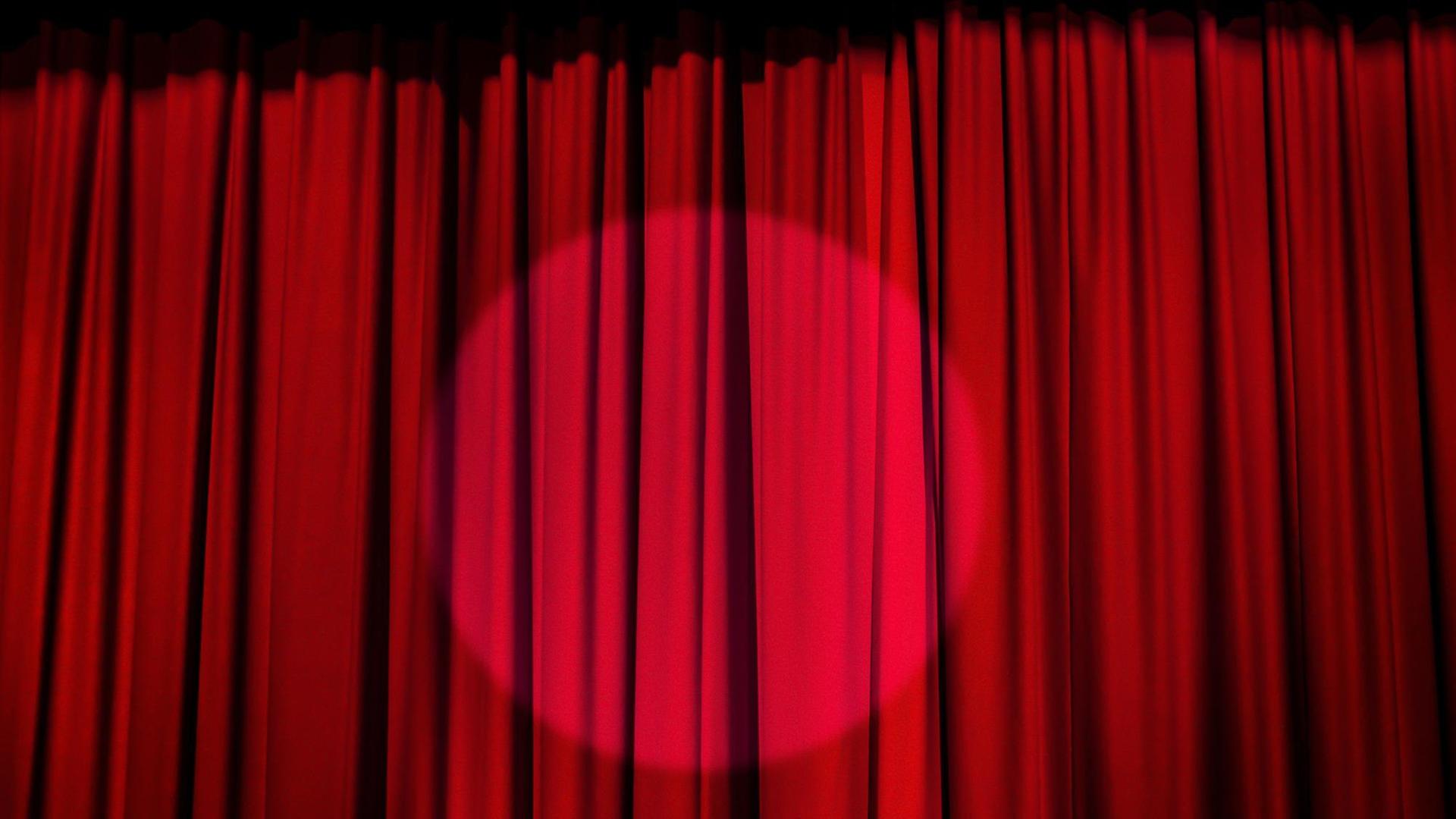 Auf dem Foto sieht man einen Scheinwerfer, auf einen roten Theater-Vorhang gerichtet. Auf dem Foto sieht man einen Scheinwerfer, auf einen roten Theater-Vorhang gerichtet.