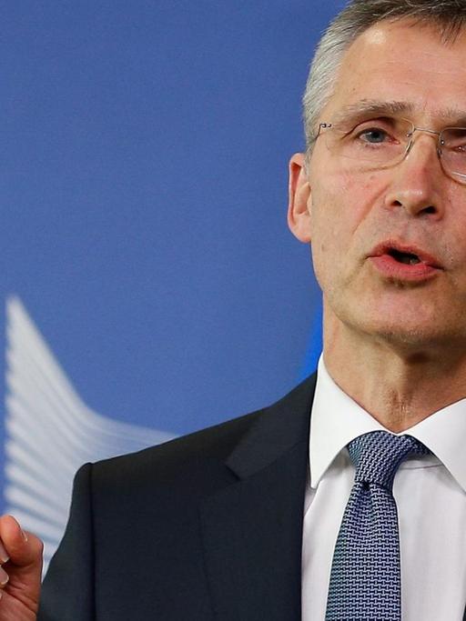 Stoltenberg steht vor einem blauen Backdrop der EU-Kommisssion, spricht und hebt den Zeigefinger.