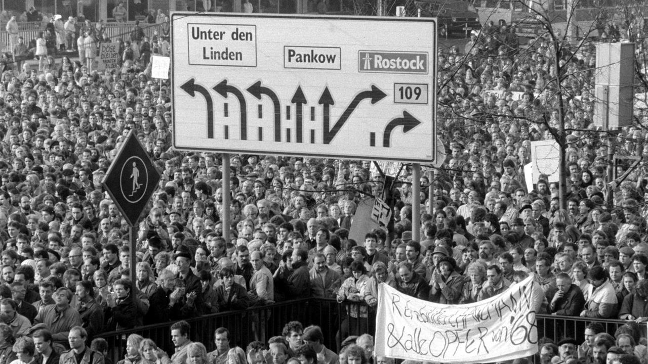 Alexanderplatz voller Menschen mit Verkehrsschild. . Es war die größte Protestdemonstration in der Geschichte der DDR. Von diesem Tag an konnte die SED-Führung an den Forderungen der Massen nicht mehr vorbeigehen. 