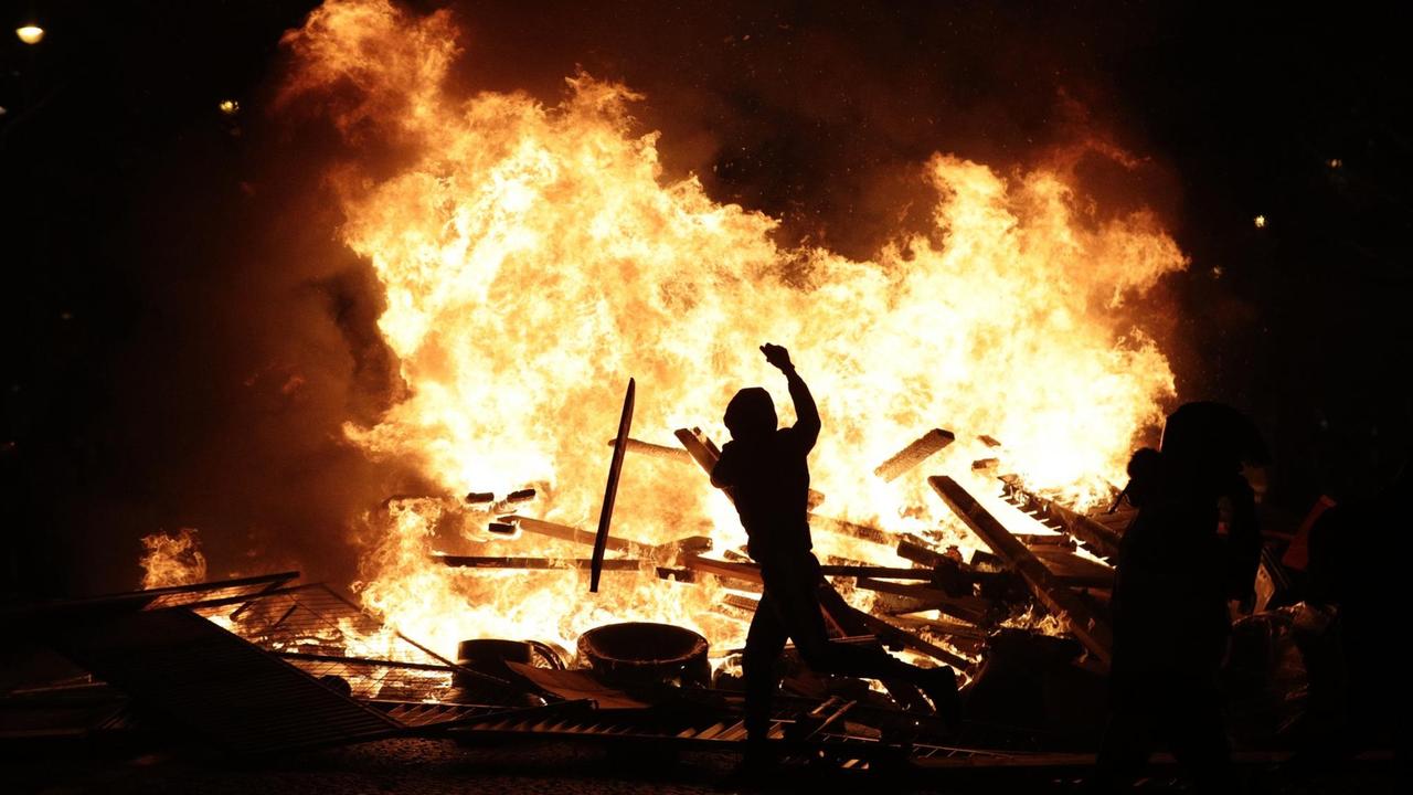 Sie sehen einen Demonstranten vor einem großen Feuer in Paris. Sie sehen einen Demonstranten vor einem großen Feuer in Paris.
