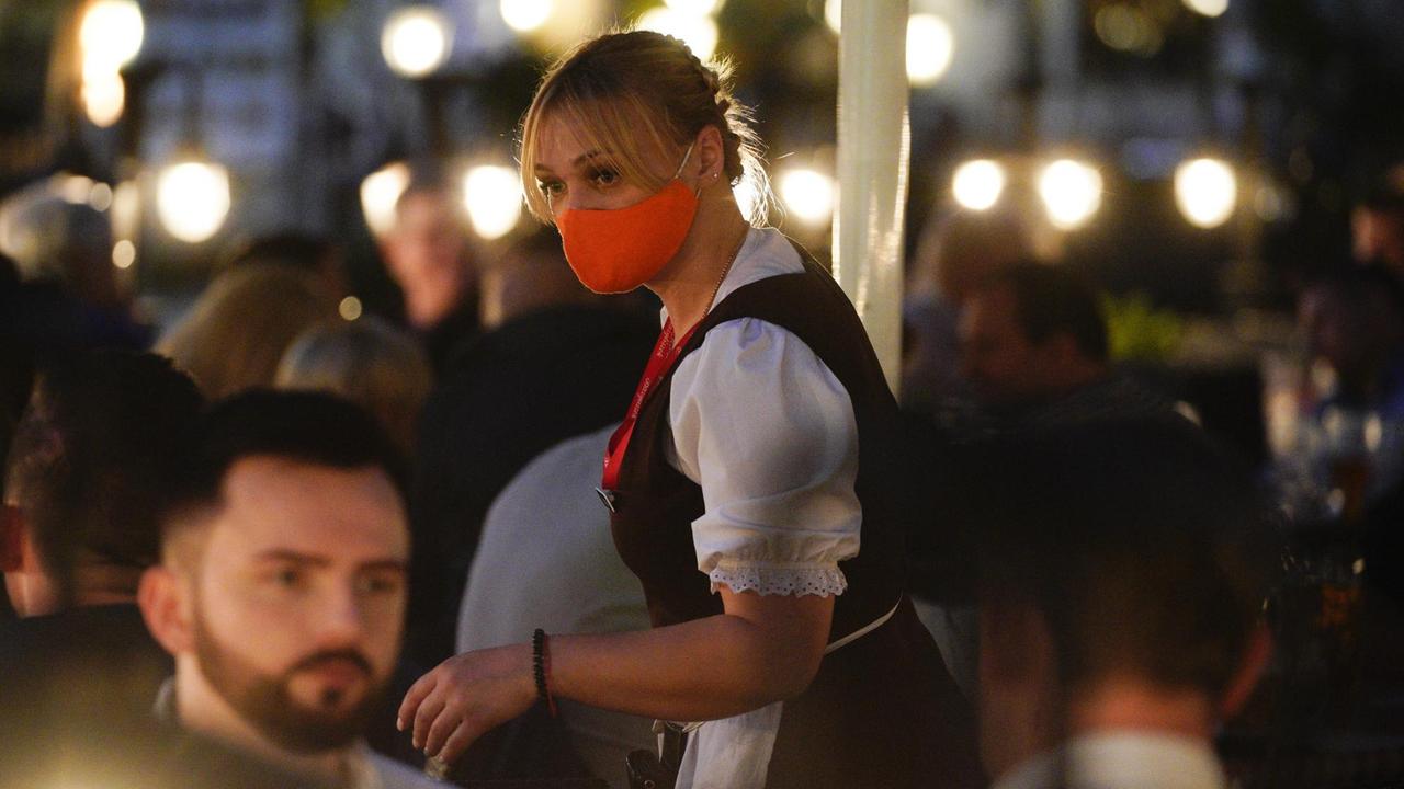 Eine Kellnerin in einer Gaststätte mit Atemschutzmaske.