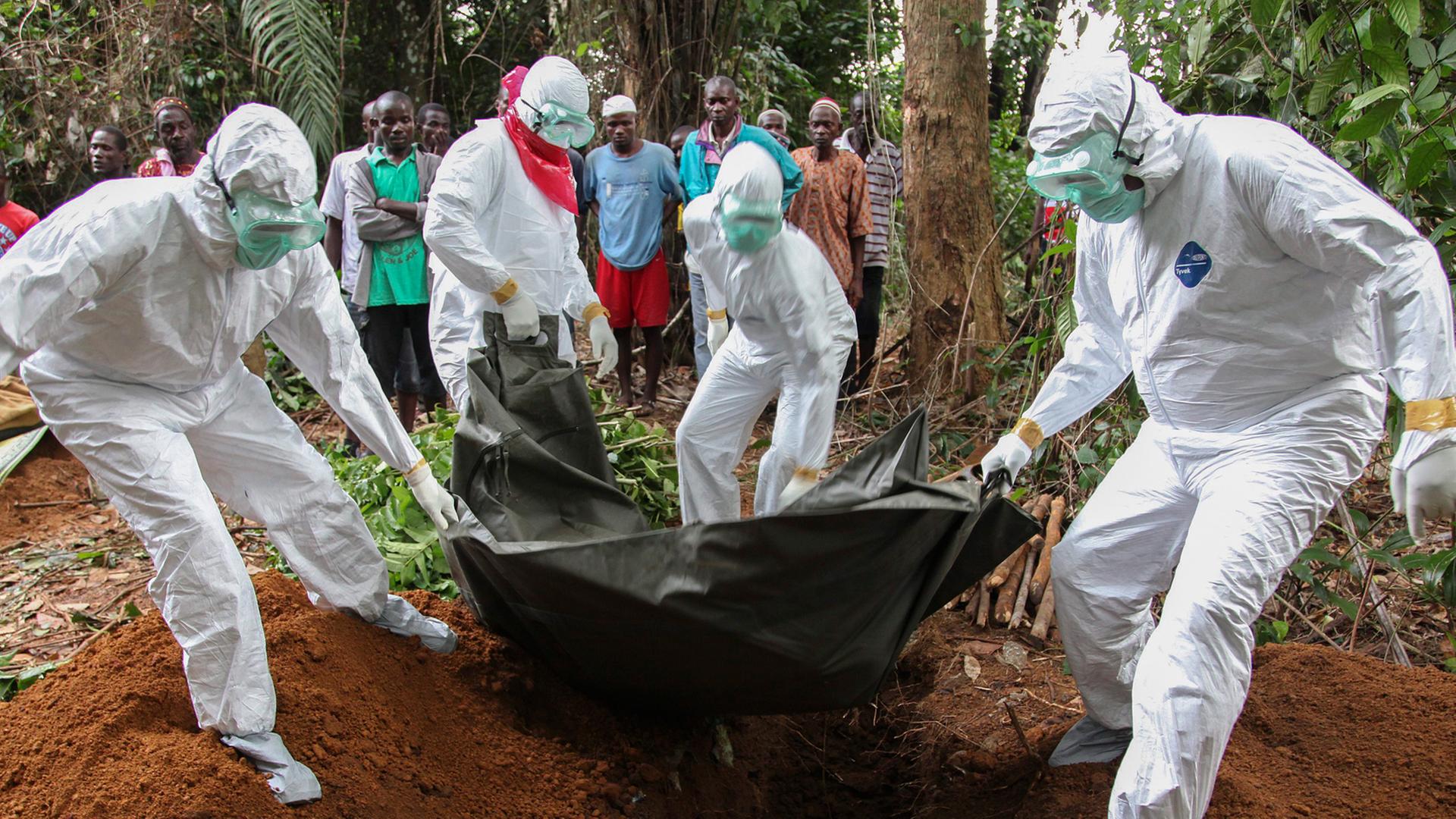 Ebola-Toter wird von Menschen in Schutzanzügen beerdigt. Ebola-Toter wird von Menschen in Schutzanzügen beerdigt.