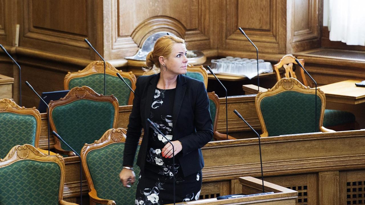 Inger Stojberg, Dänemarks Ministerin für Integration, rote Haare, schwarz-weißes Kostüm, geht zwischen Stühlen im Parlament entlang. Inger Stojberg, Dänemarks Ministerin für Integration, rote Haare, schwarz-weißes Kostüm, geht zwischen Stühlen im Parlament entlang.