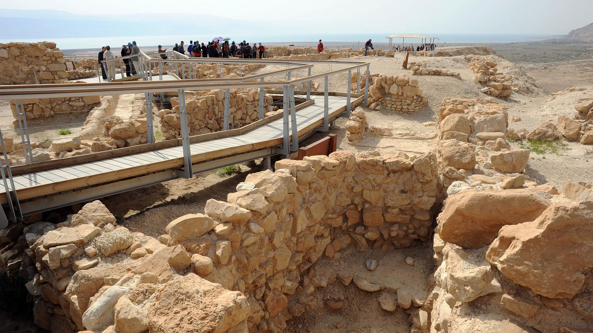 Touristen laufen auf einem Holzsteg über die Ausgrabungsstätte Qumran.