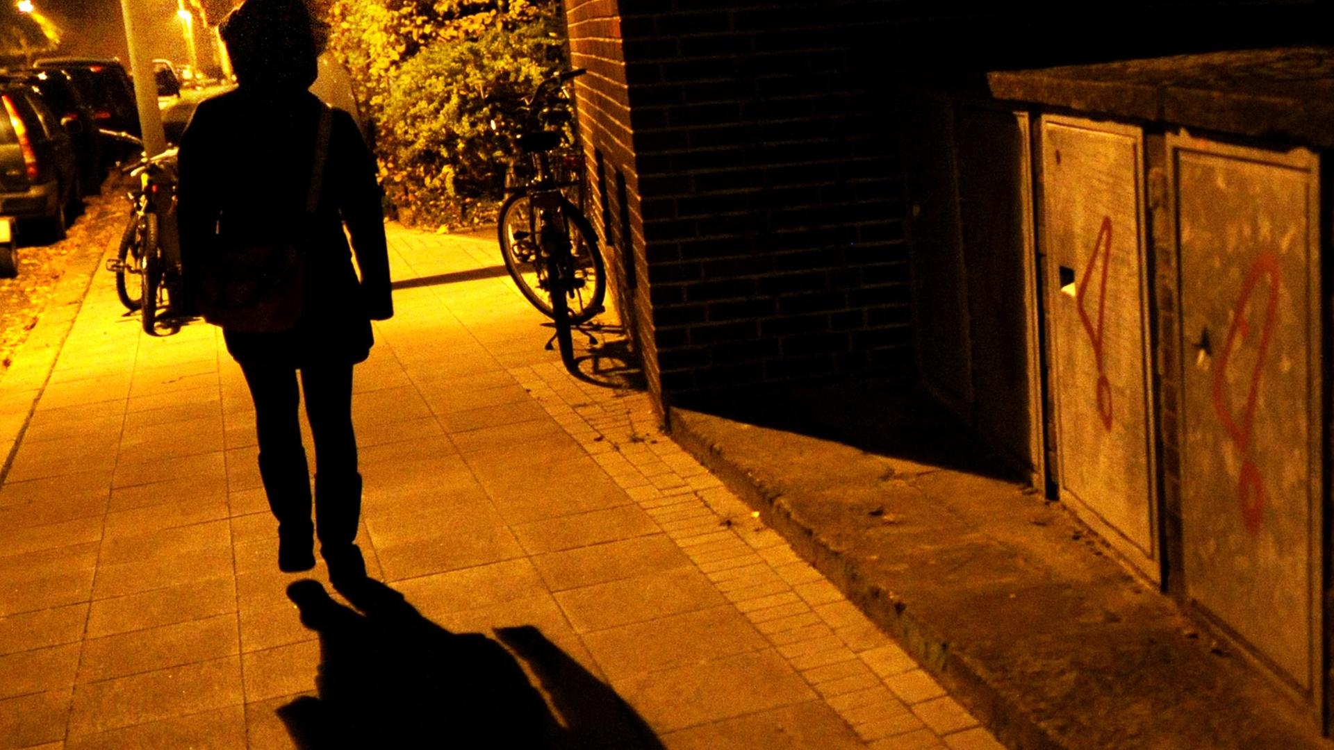 Eine Frau geht im Licht der Straßenlaternen alleine über eine dunkle Straße Eine Frau geht im Licht der Straßenlaternen alleine über eine dunkle Straße