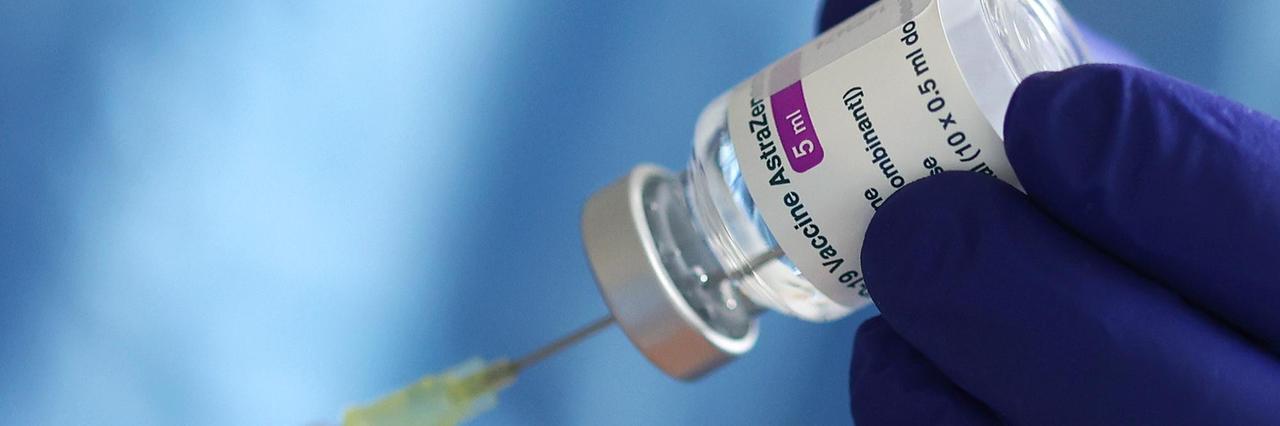 Ein blau behandschuhte Hand hält ein Fläschchen mit dem Covid-Impfstoff von AstraZeneca und präpariert eine Spritze. Ein blau behandschuhte Hand hält ein Fläschchen mit dem Covid-Impfstoff von AstraZeneca und präpariert eine Spritze.
