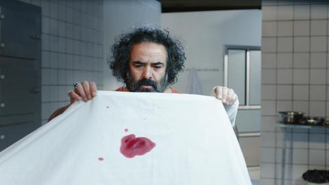 Ein Mann hält ein mit Blut beflecktes weißes Laken in Händen. Filmstill aus Mani Haghighis "Khook"