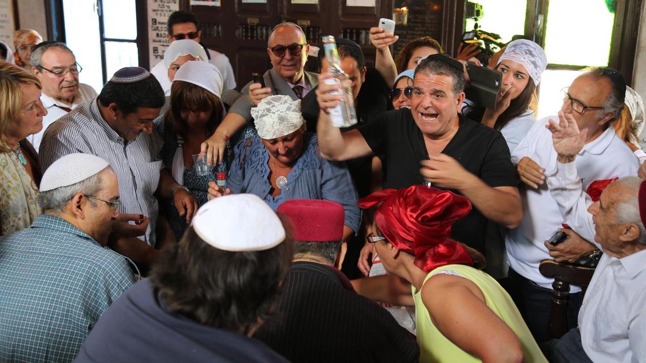 Eine Gruppe von Menschen in der Synagoge La Ghriba auf der tunesischen Insel Djerba. Ein Mann hält eine Flasche mit Feigenschnaps, auf Djerba "Boukha" genannt, in die Höhe. Der Schnaps ist Teil eines Rituals, das zum jüdischen Fest Lag baOmer gehört. Foto: imago stock&people Eine Gruppe von Menschen in der Synagoge La Ghriba auf der tunesischen Insel Djerba. Ein Mann hält eine Flasche mit Feigenschnaps, auf Djerba "Boukha" genannt, in die Höhe. Der Schnaps ist Teil eines Rituals, das zum jüdischen Fest Lag baOmer gehört. Foto: imago stock&people