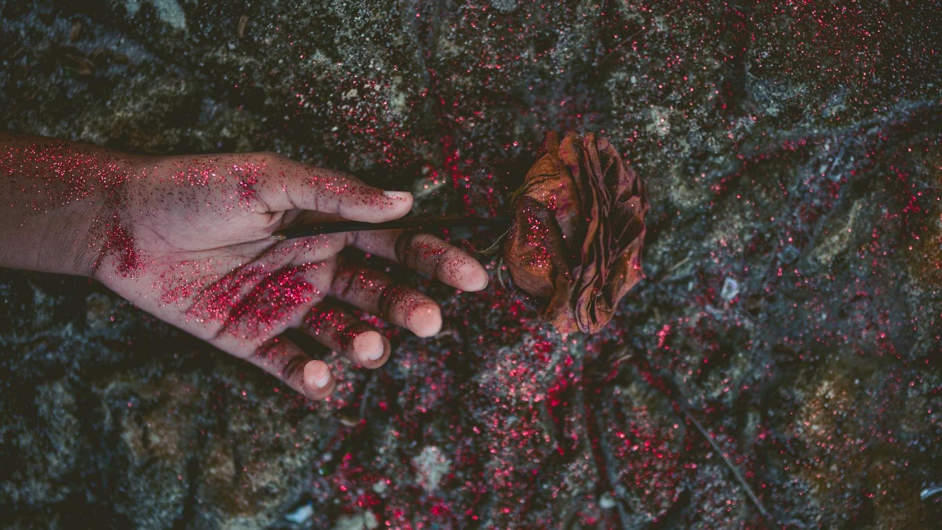 Eine Hand mit einer verwelkten Rose liegt auf dem Boden. Eine Hand mit einer verwelkten Rose liegt auf dem Boden.