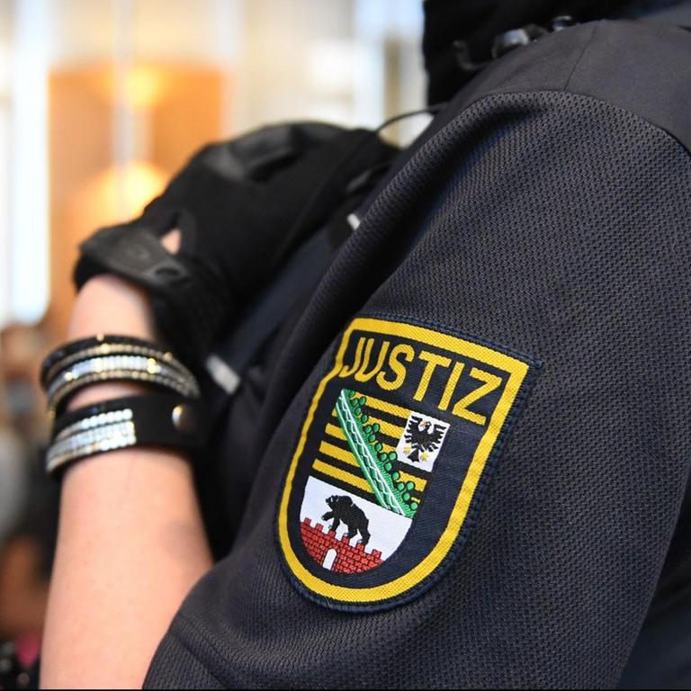 Eine Justizbeamtin wartet im Landgericht Magdeburg auf den Prozessbeginn. Auf ihrem Arm ist das Wappen der sächsischen Justiz zu sehen.