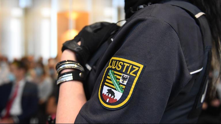 Eine Justizbeamtin wartet im Landgericht Magdeburg auf den Prozessbeginn. Auf ihrem Arm ist das Wappen der sächsischen Justiz zu sehen.