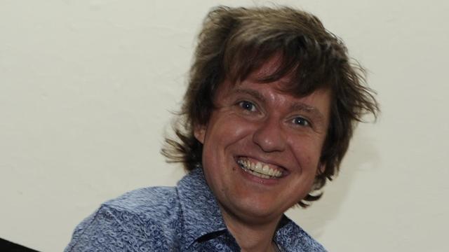 Komponist Michael Edwardsträgt ein blau gemustertes Hemd und lacht in die Kamera