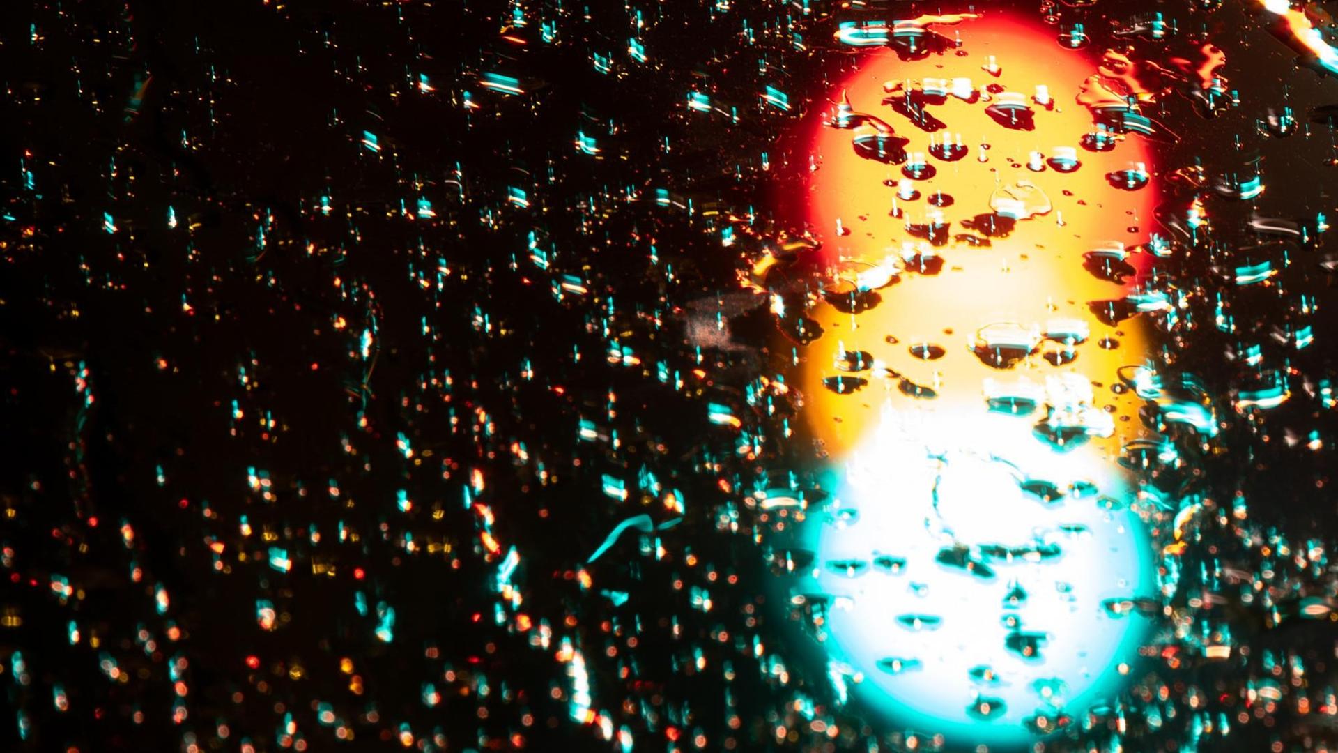 Eine Ampel leuchtet in allen Phasen Rot, Gelb und Grün. Über dem durch Langzeitbelichtung entstandenen Foto liegen Regentropfen. Eine Ampel leuchtet in allen Phasen Rot, Gelb und Grün. Über dem durch Langzeitbelichtung entstandenen Foto liegen Regentropfen.