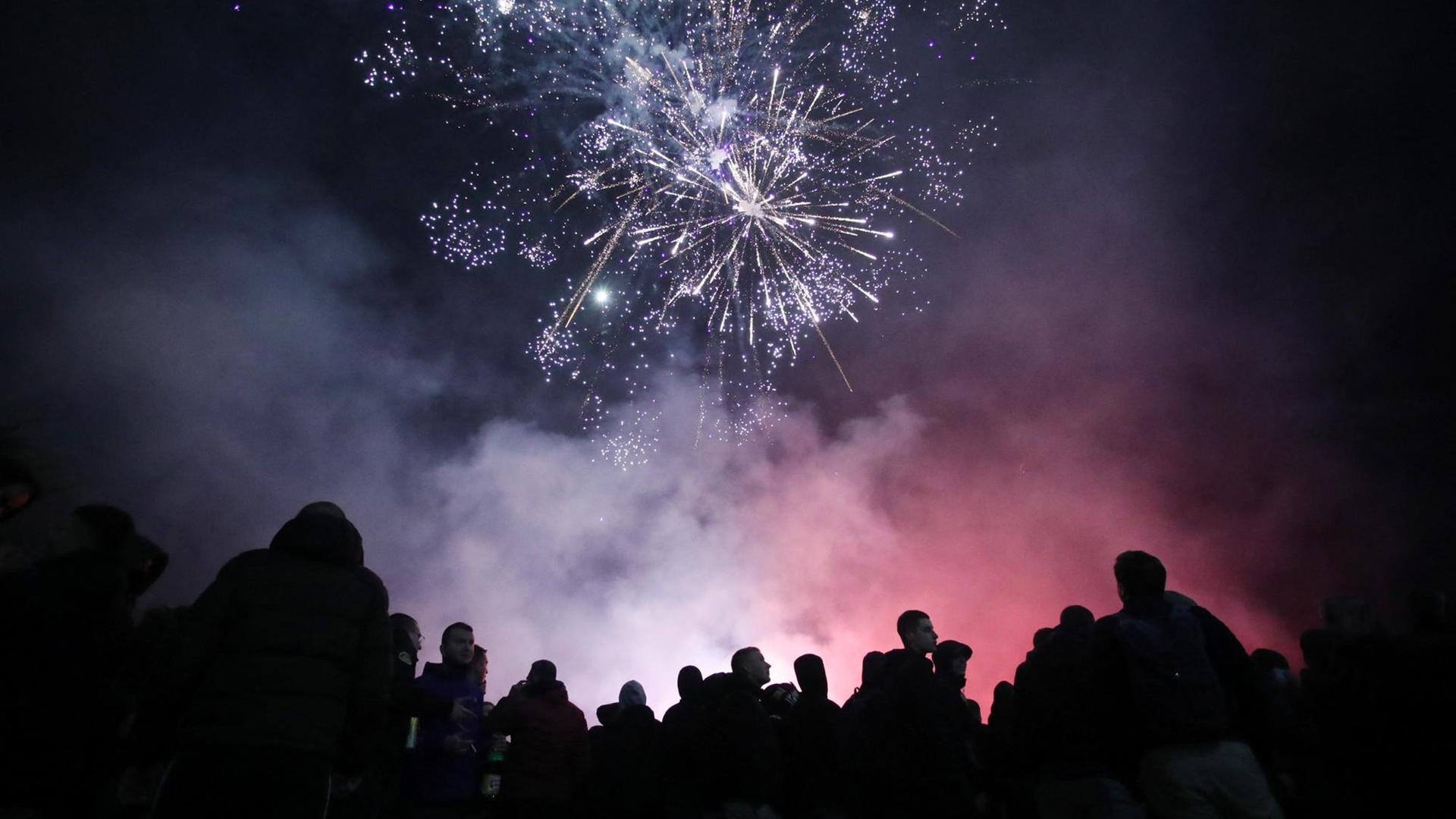 Die Silhouetten von Menschen heben sich unter rotem und blauem Feuerwerk ab. Die Silhouetten von Menschen heben sich unter rotem und blauem Feuerwerk ab.