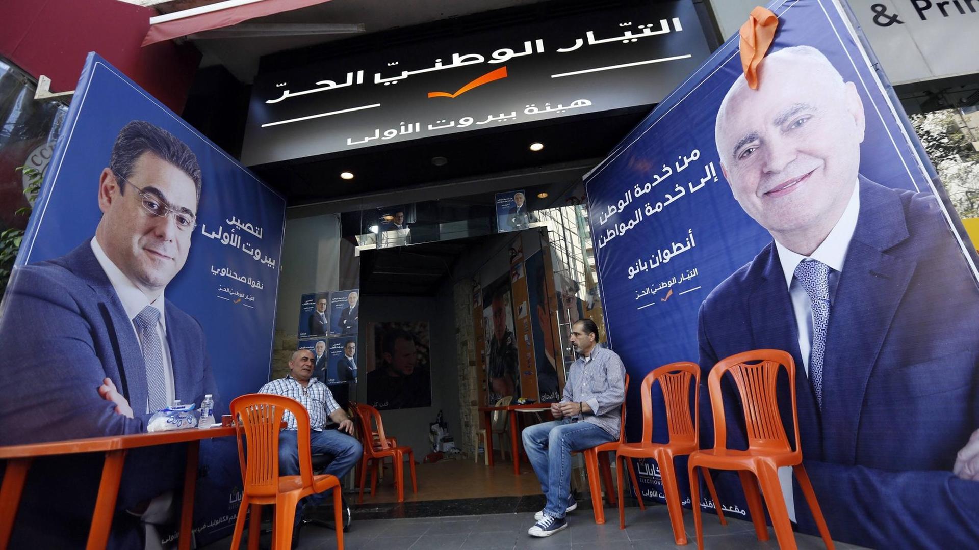 Zwei Männer sitzen vor einem Laden in Beirut, vor dem Wahlplakate für die bevorstehenden Parlamentswahlen am 6. Mai stehen