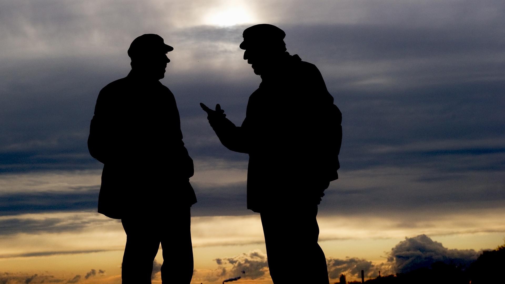 Zwei Männer unterhalten sich vor einem farbenprächtigen Abendhimmel. Zwei Männer unterhalten sich vor einem farbenprächtigen Abendhimmel.