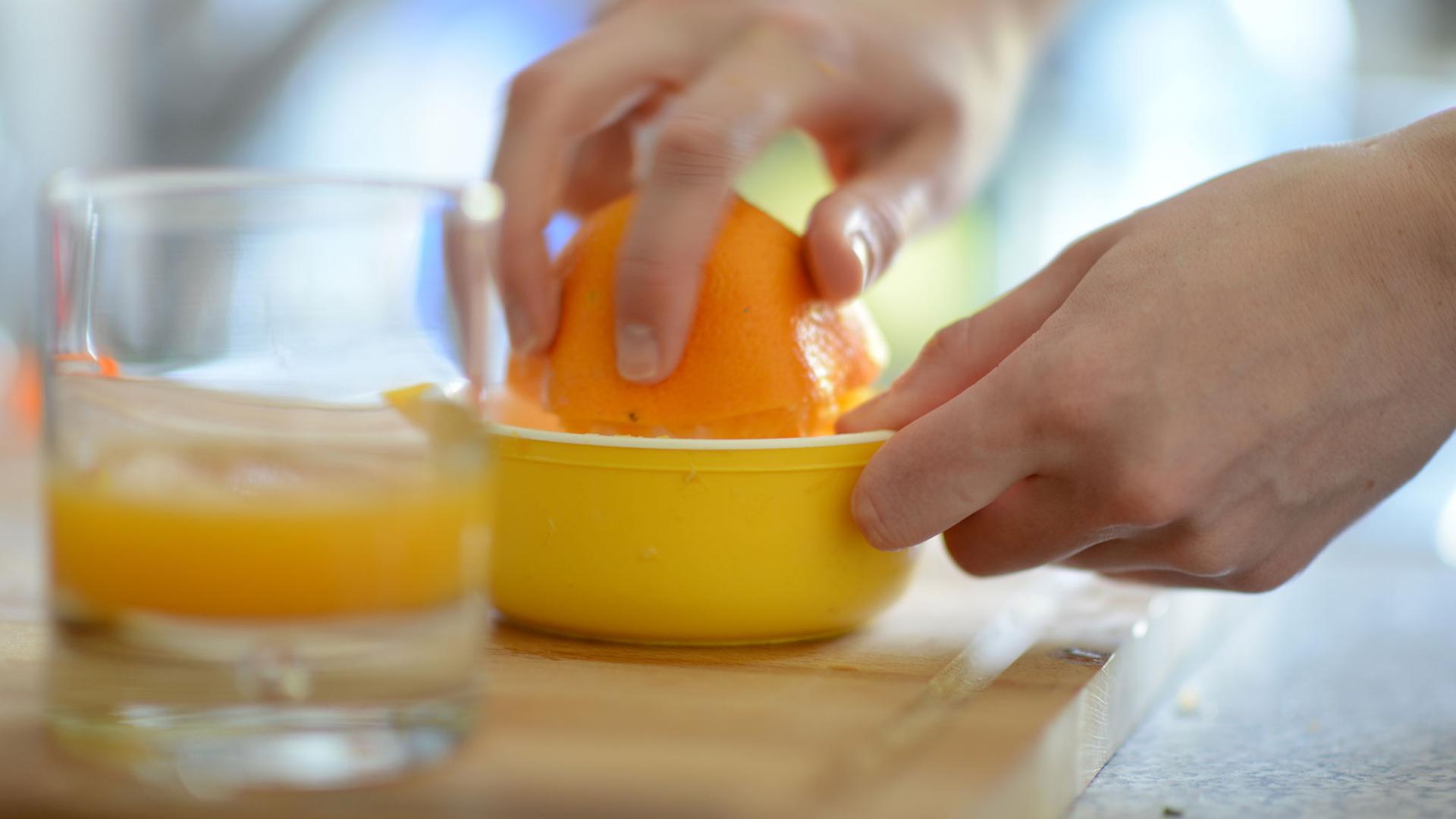 Eine Frau presst eine Orange aus, im Vordergrund ein Glas mit Orangensaft. Eine Frau presst eine Orange aus, im Vordergrund ein Glas mit Orangensaft.