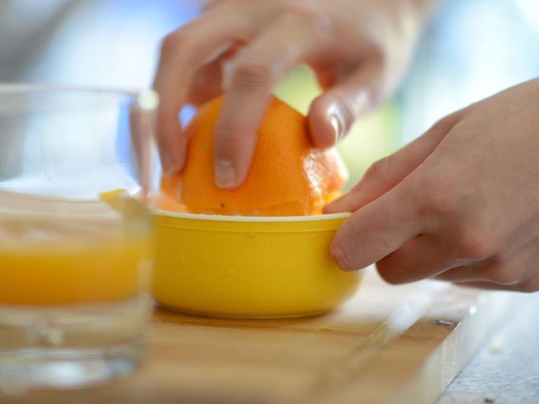 Eine Frau presst eine Orange aus, im Vordergrund ein Glas mit Orangensaft.