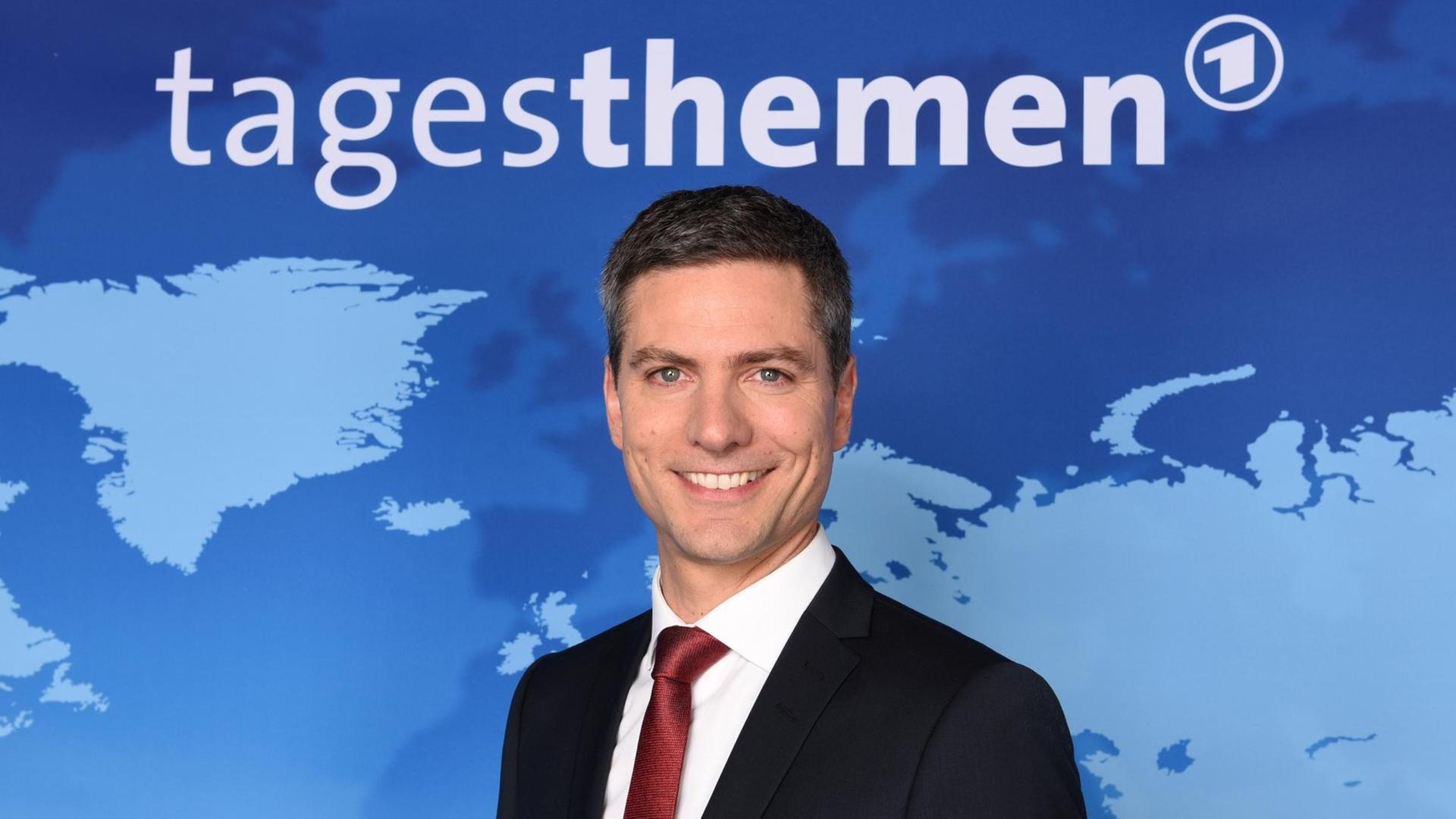 Tagesthemen-Moderator Ingo Zamperoni lächelt bei einem Fototermin vor dem Hintergrund der Nachrichtensendung