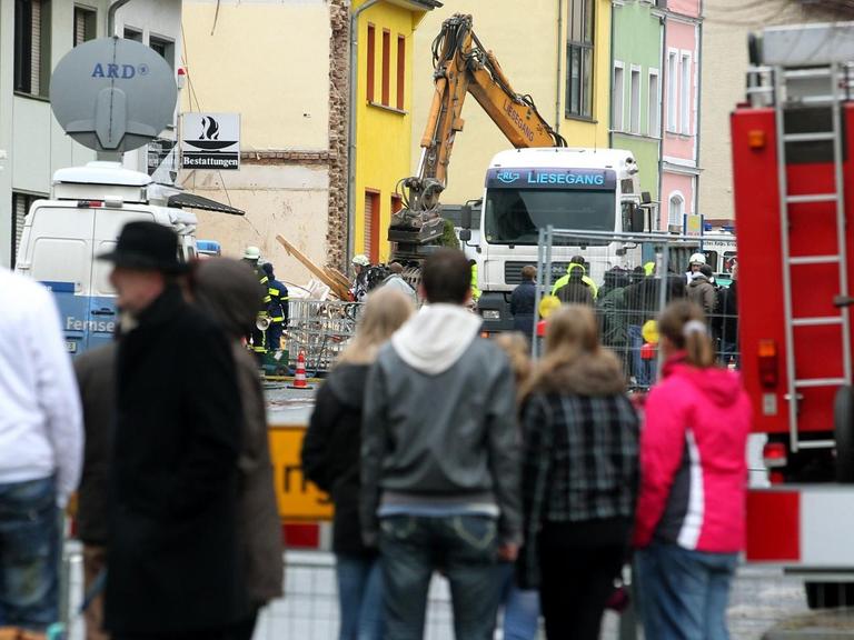 Schaulustige gucken hinter einer Absperrung zum explodierten Wohnhaus in Brühl.