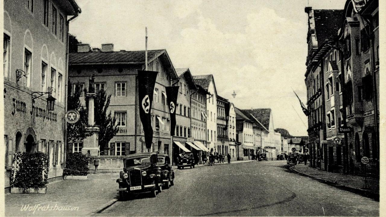 Eine Postkarten mit Straßenansicht, Autos und Fahnen mit den Symboliken der Nationalsozialisten in Wolfratshausen Isartal.